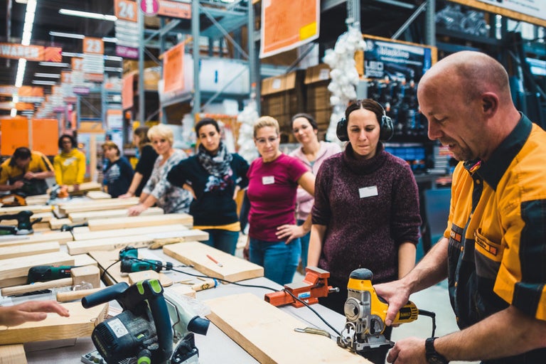 Grupp av människor deltar i en träbearbetningskurs med elverktyg.