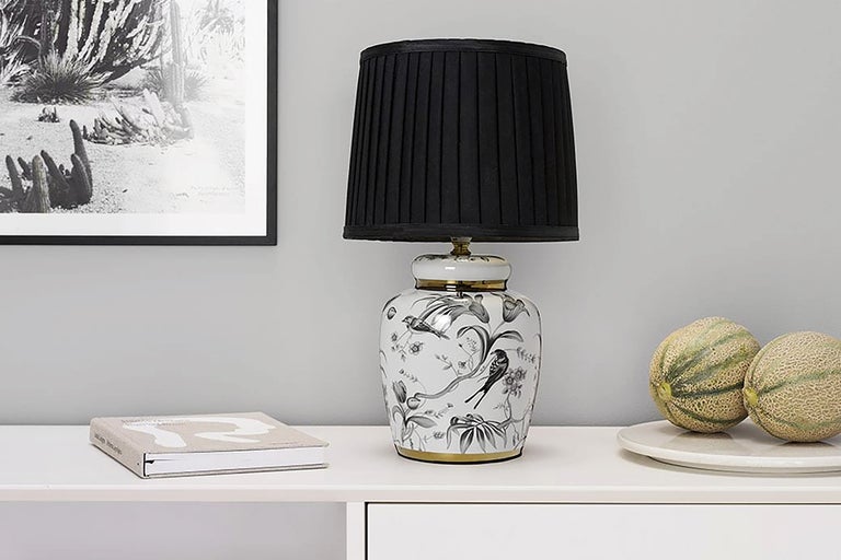 Dekorativ bordslampa med fågelmotiv och svart lampskärm på ett bord