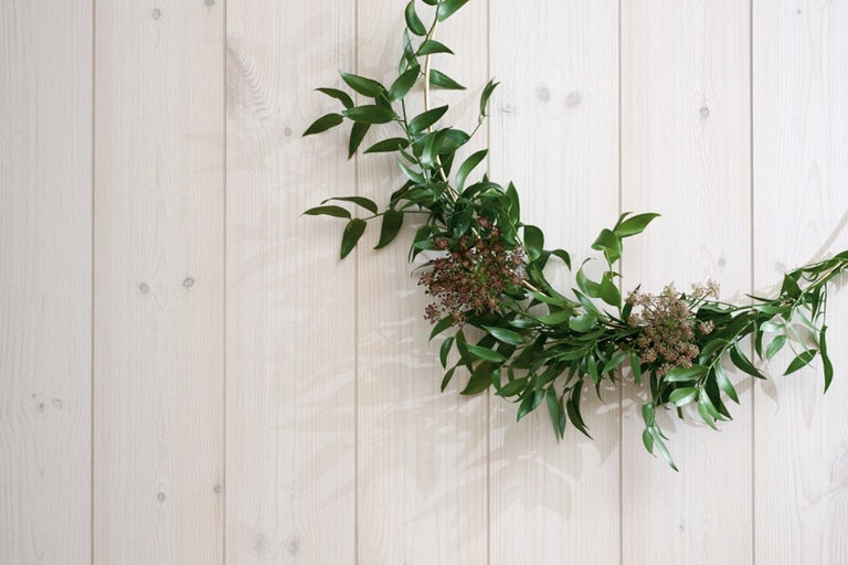 Halvcirkelformad blomsterkrans med gröna blad och små blommor på en trävägg