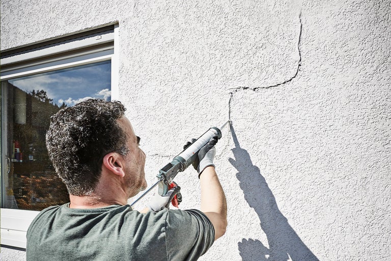 Man tätar spricka i husvägg med tätningsmedel