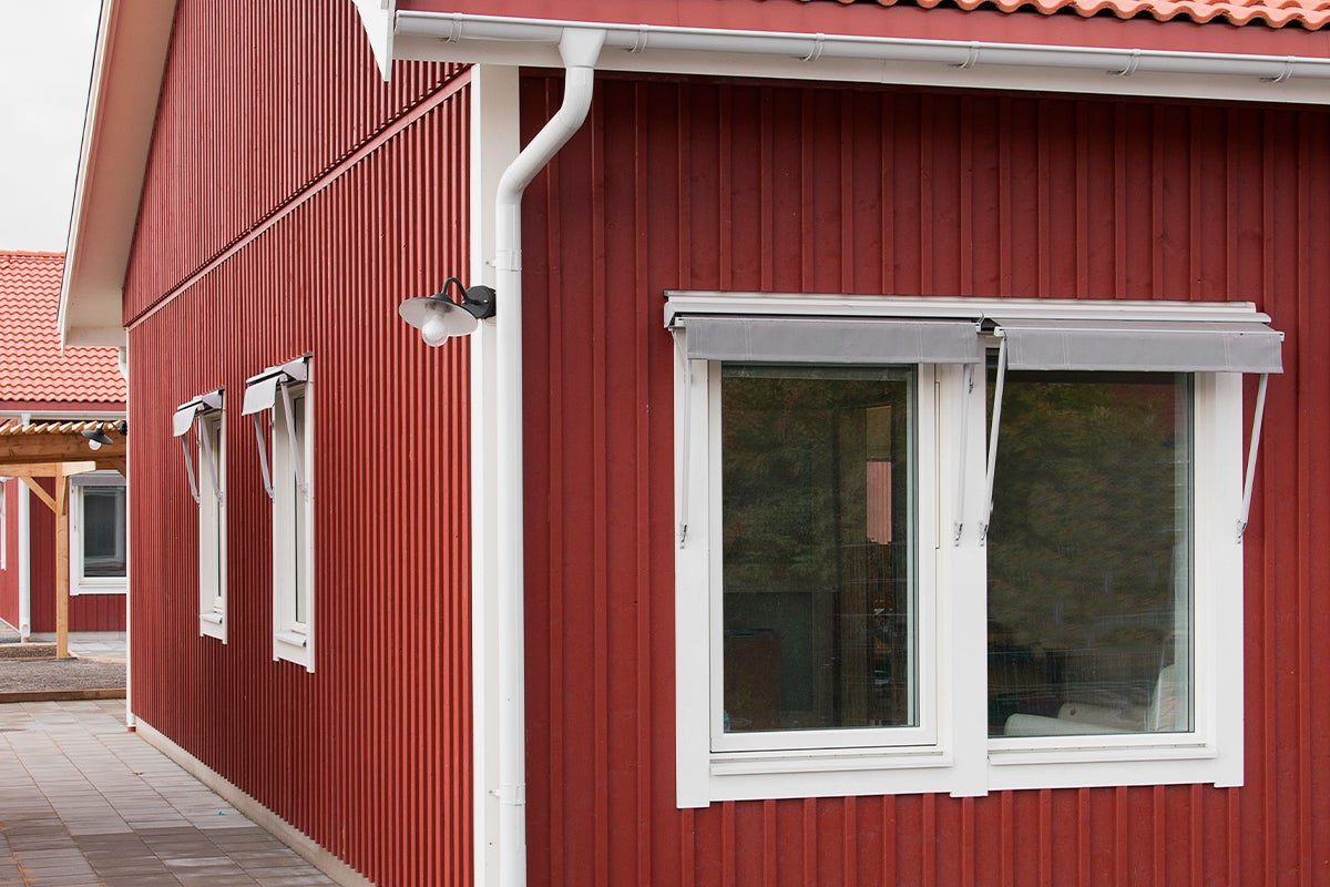 Exteriör av ett hus med träfasad, fönster med markiser och stuprör