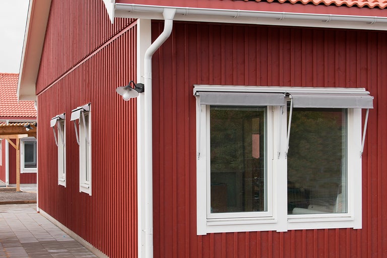 Exteriör av ett hus med träfasad, fönster med markiser och stuprör