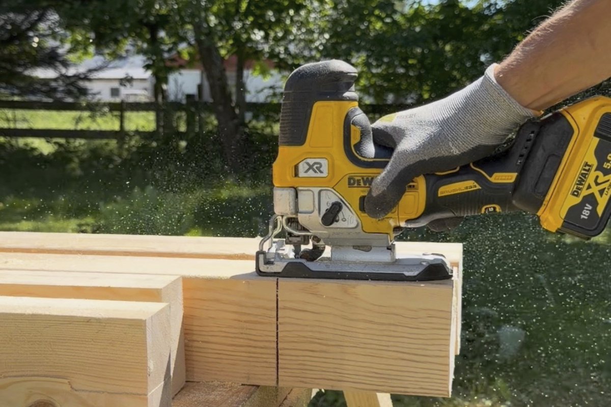 En person använder en batteridriven Dewalt sticksåg för att såga i en träbjälke utomhus.
