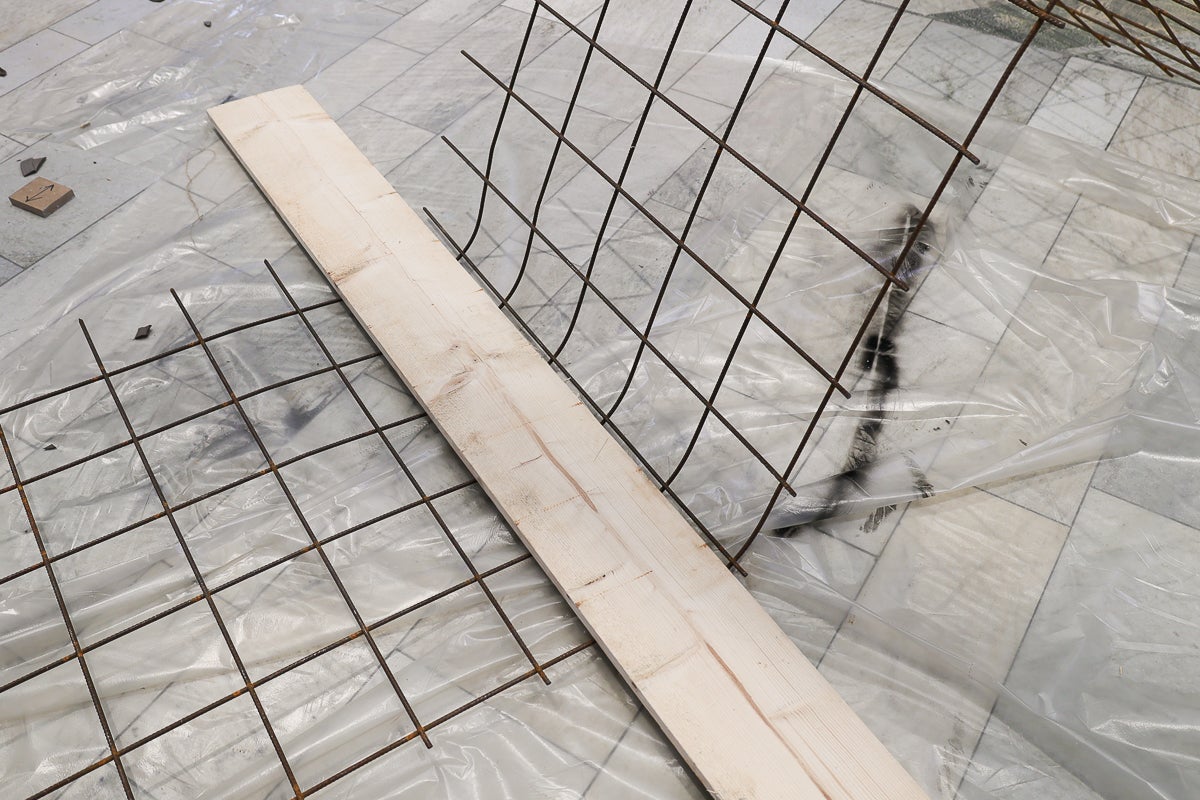 Armeringsnät böjs med en formbräda på en byggarbetsplats, skyddad av plastfilm på ett klinkergolv.