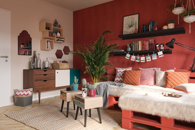 Vardagsrum med röd vägg, soffa av lastpallar, byrå och dekoration