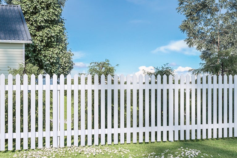 Vy över ett vitt staket framför ett hus och träd under en blå himmel