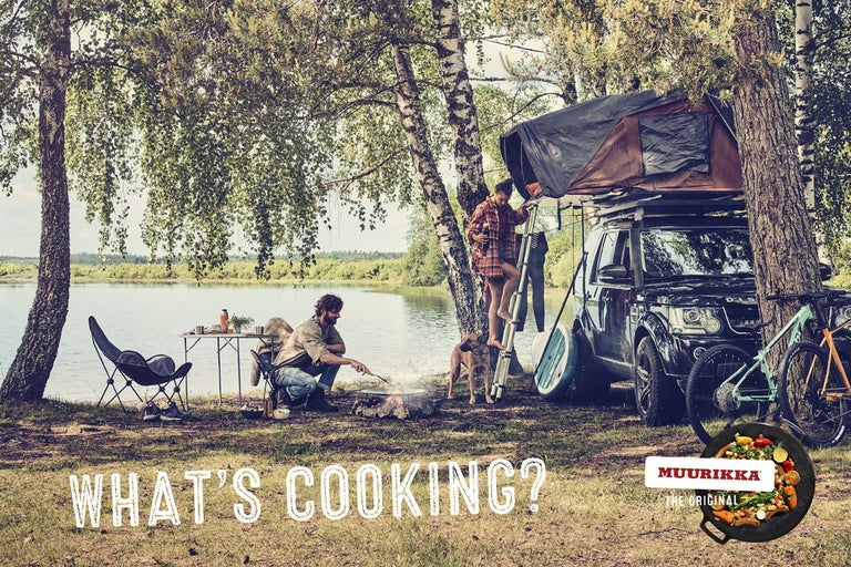 Campingplats vid sjön med bil, taktält, campingmöbler och människor