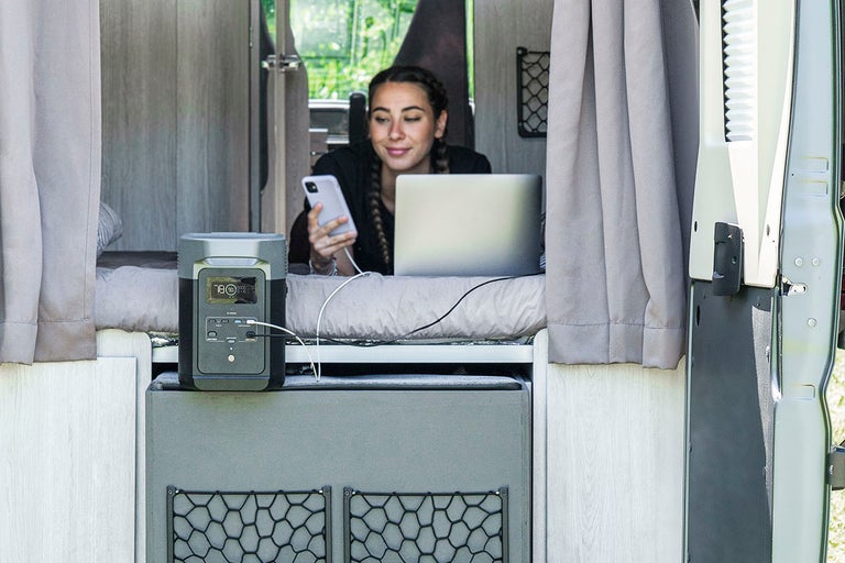 Kvinna använder bärbar kraftstation i husbil för att ladda bärbar dator och smarttelefon