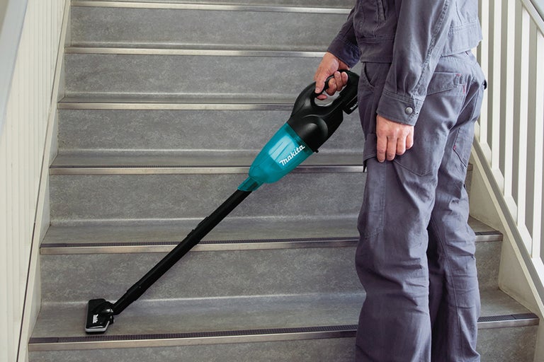 En person använder en batteridriven dammsugare på en trappa. Dammsugaren har ett fogmunstycke.