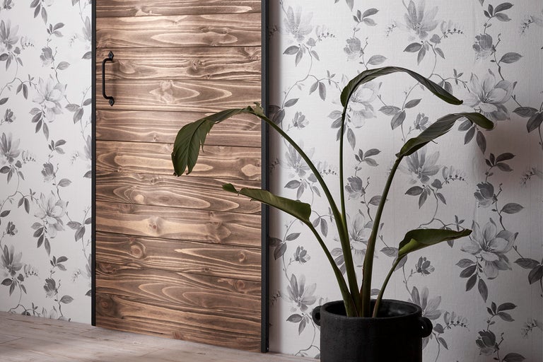 Skjutdörr i trä bredvid krukväxt och blommig tapet