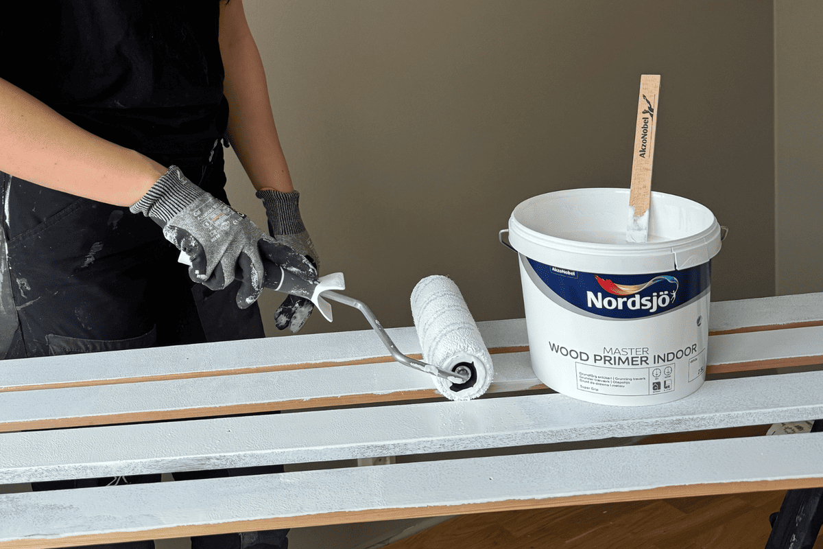 Person grundar träribbor med färgroller och Nordsjö trägrundfärg för inomhusbruk