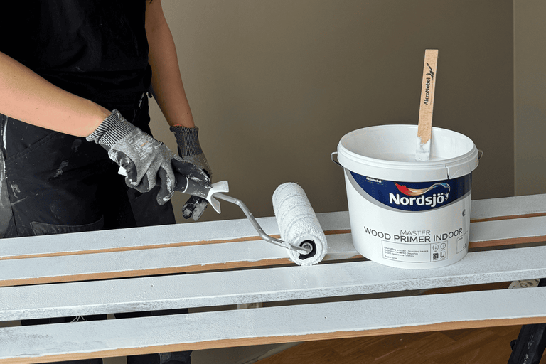 Person grundar träribbor med färgroller och Nordsjö trägrundfärg för inomhusbruk