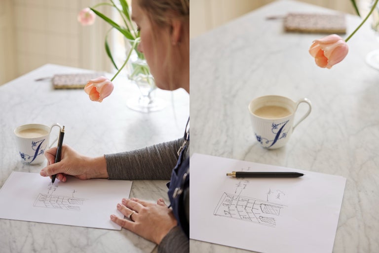 En person skissar en rumsplanering på vitt papper vid ett marmorbord med en kaffekopp och en tulpan.