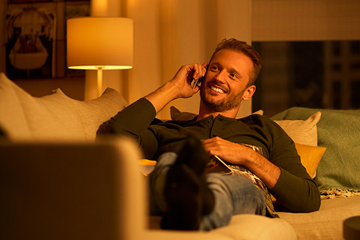 Man pratar i telefon på en soffa i vardagsrummet under en golvlampa.