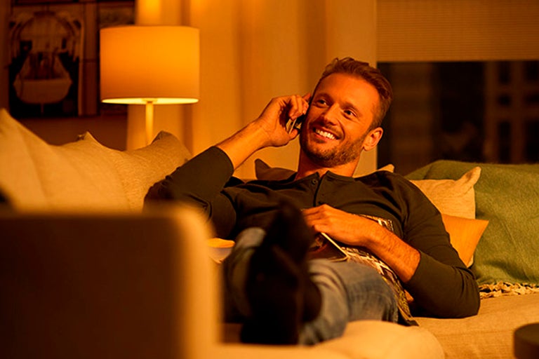 Man pratar i telefon på en soffa i vardagsrummet under en golvlampa.