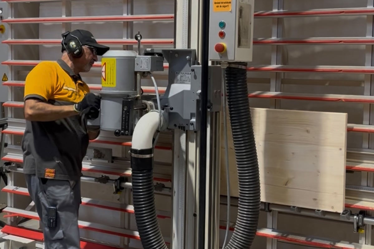 En man använder en stående panelsåg med utsugningsanordning i en verkstad.