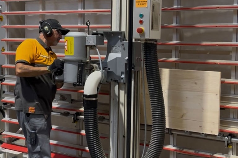 En man använder en stående panelsåg med utsugningsanordning i en verkstad.