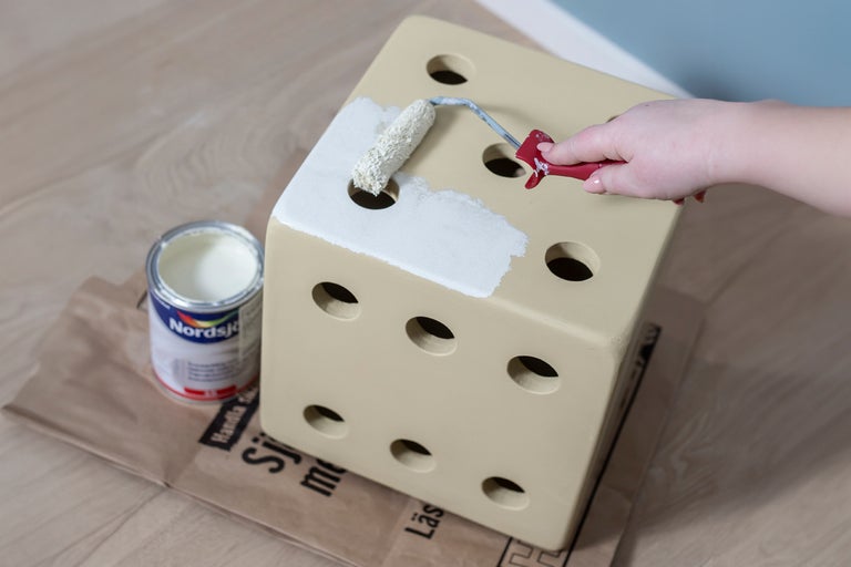 Tärningsformad pall målas med roller, färgburk står bredvid