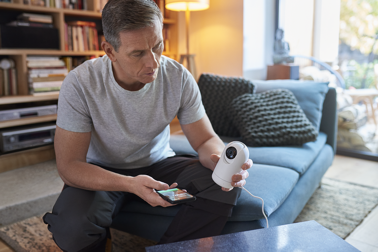 Man sitter i vardagsrummet och styr en övervakningskamera med sin smarttelefon