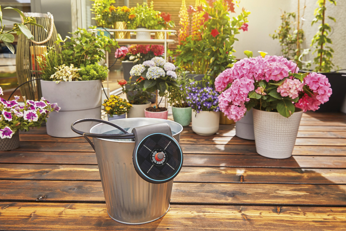 Automatisk bevattning i hink framför blommor på balkongen