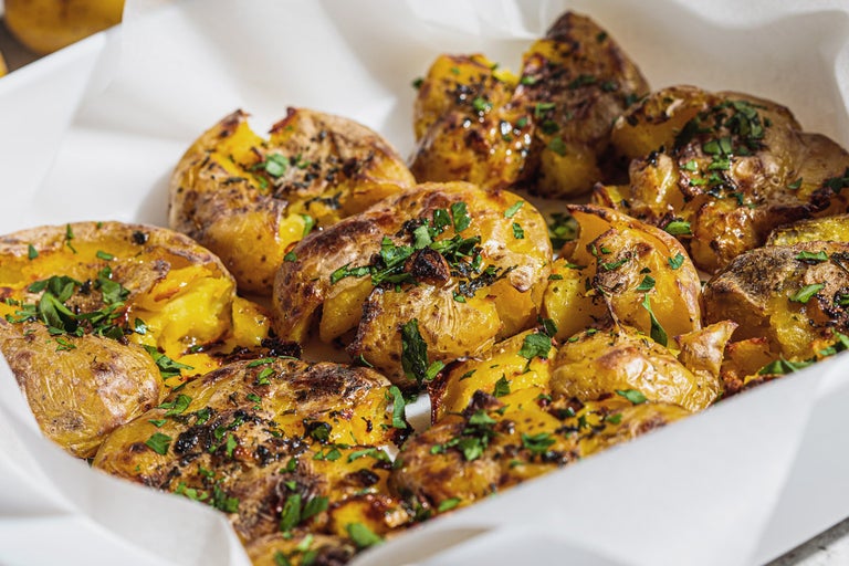 Närbild av krossad potatis i en skål, garnerad med örter.