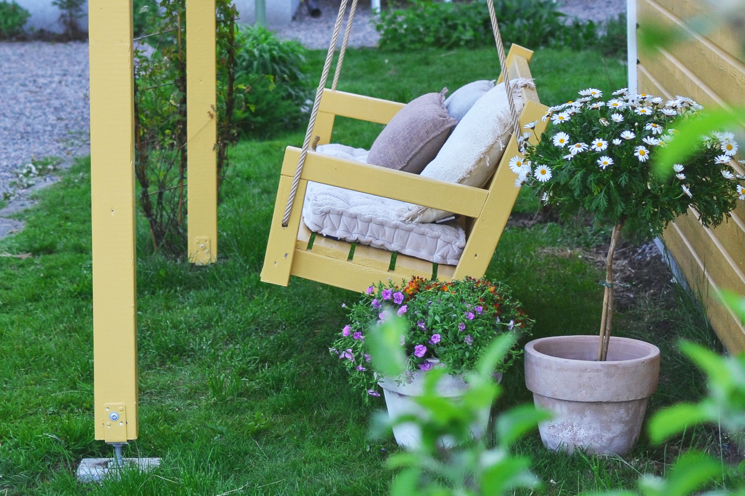 Trädgårdsscen med en gul träsving, dekorativa kuddar och blomkrukor
