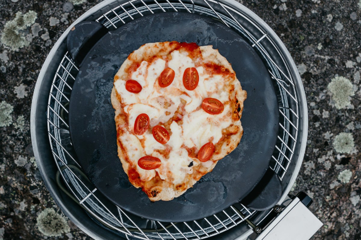 Pizza med tomater och ost på en pizzasten i grillen