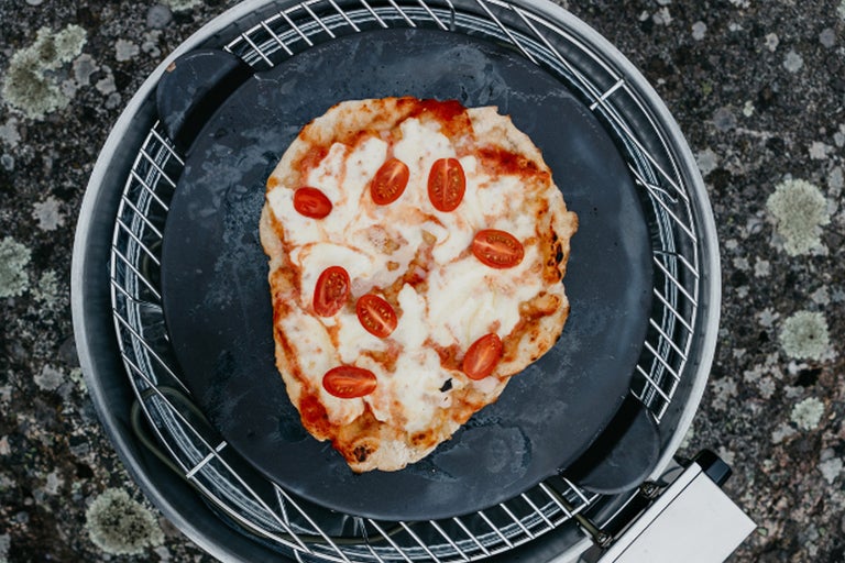 Pizza med tomater och ost på en pizzasten i grillen
