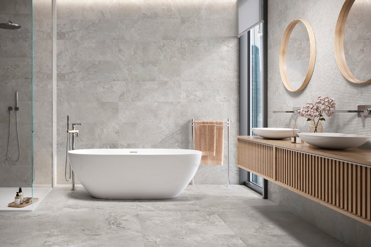 Modernt badrum med grå kakel, fristående badkar, tvättställ och runda speglar