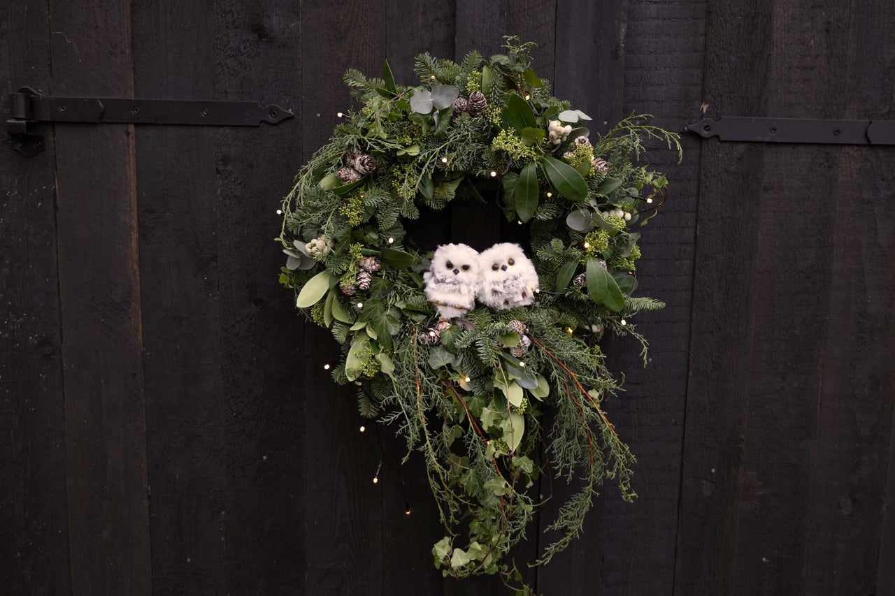 Dekorativ dörrkrans med växter, kottar, ljus och två dekorativa ugglor