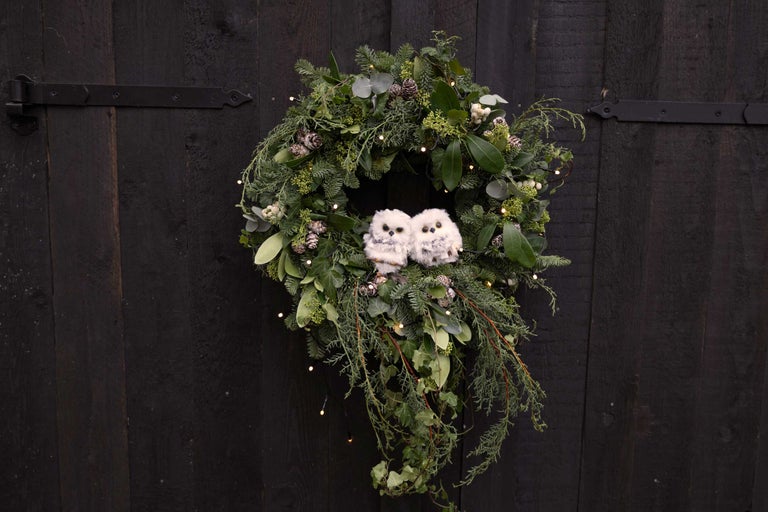 Dekorativ dörrkrans med växter, kottar, ljus och två dekorativa ugglor