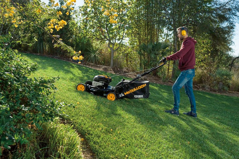 Man klipper gräs med en McCulloch gräsklippare i en trädgård.