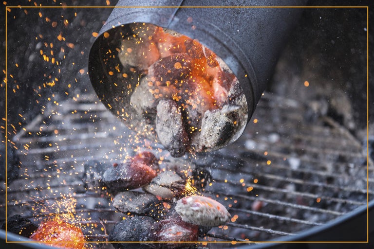 Brinnande grillkol hälls från en skorstenständare i en grill.