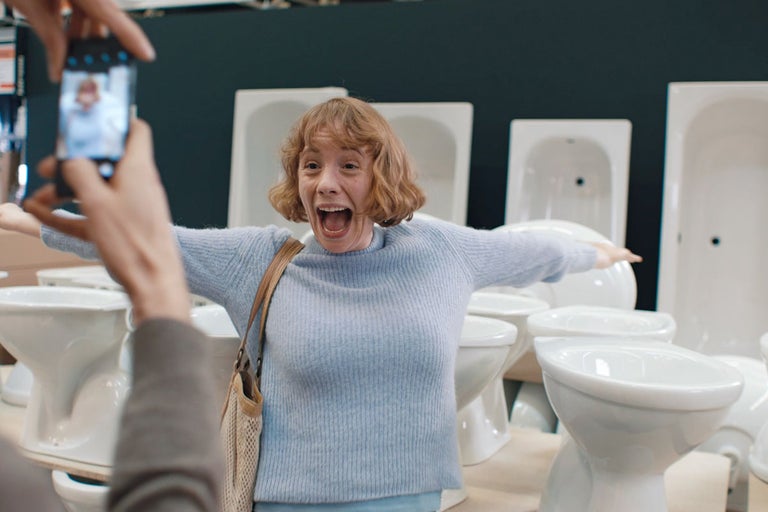 Kvinna poserar entusiastiskt framför toaletter och badkar i en järnaffär för ett foto.