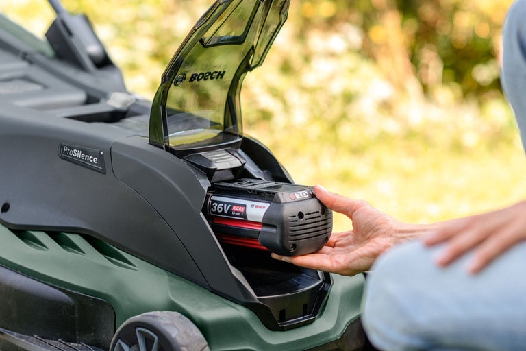 En person sätter in ett 36 volts batteri i en Bosch gräsklippare.