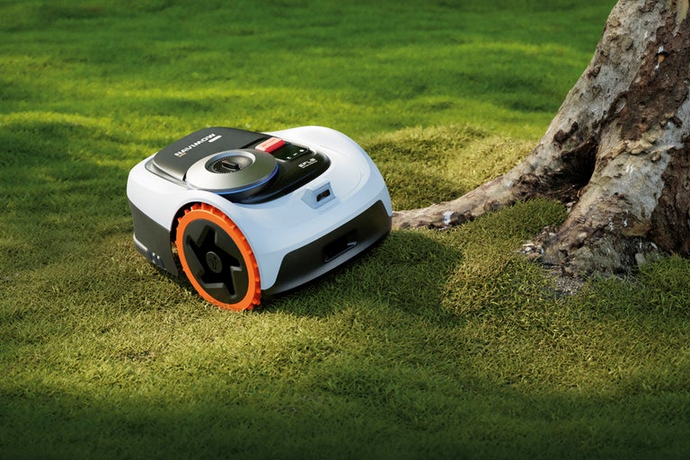 Robotgräsklippare på gräsmatta bredvid ett träd