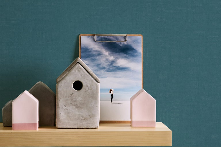 Dekorativa hus av betong och keramik på en hylla med ett klippbord i bakgrunden.