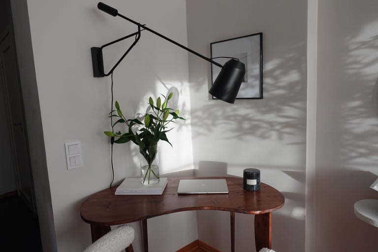 Skrivbord med svängarmslampa, bärbar dator och blomvas i ett ljust rum