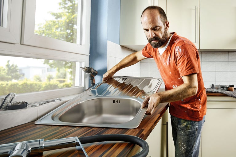 En rörmokare installerar en diskho i rostfritt stål i en köksbänk.