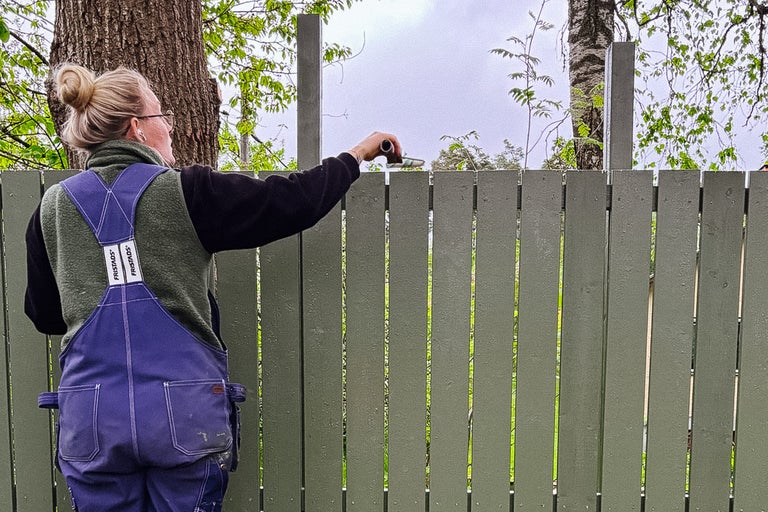 Kvinna målar trästaket med pensel