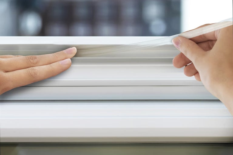 En person fäster en fönstertätning på fönsterkarmen.