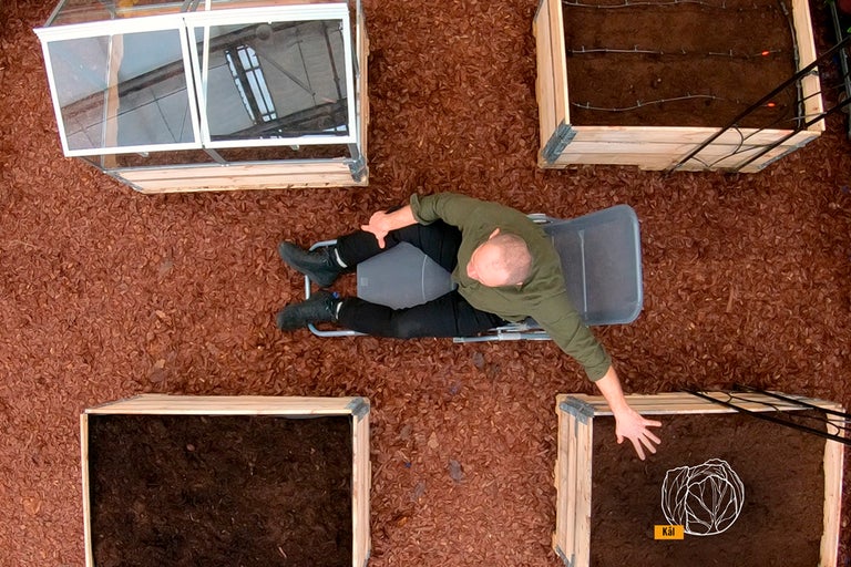 Översikt av en man som ligger på en solstol i en trädgård med upphöjda rabatter och ett drivhus