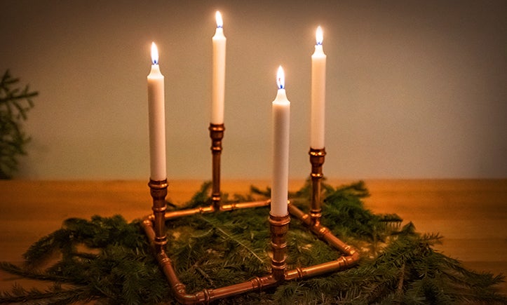 Adventskrans med fyra brinnande ljus och kopparrörsram på grangrönska