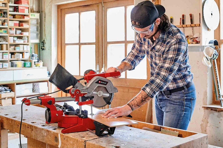 En man skär trä med en Einhell kap- och geringssåg i en verkstad.