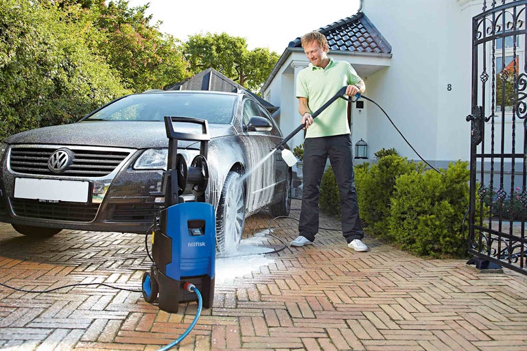 En man rengör en bil med en Nilfisk högtryckstvätt på en uppfart.