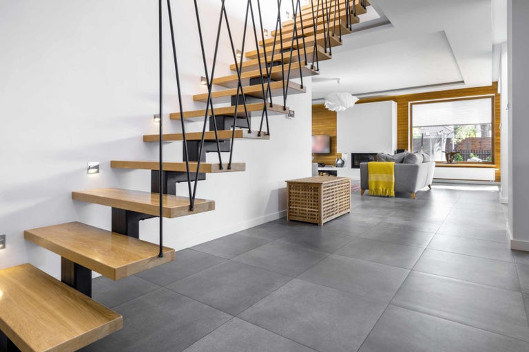 Modernt vardagsrum med trappa, grått golv och trädetaljer.