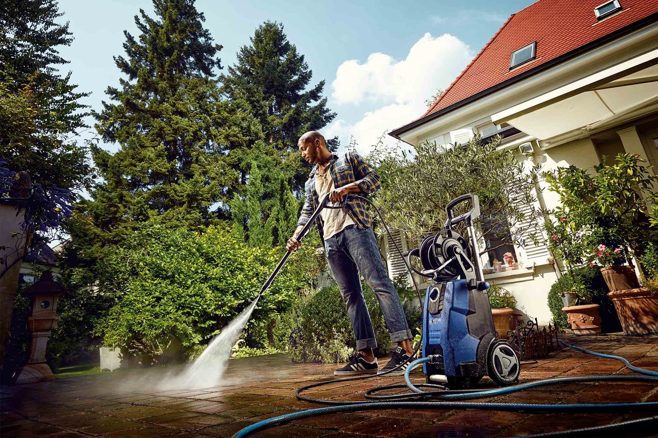 Man rengör en terrass framför ett hus med en högtryckstvätt.