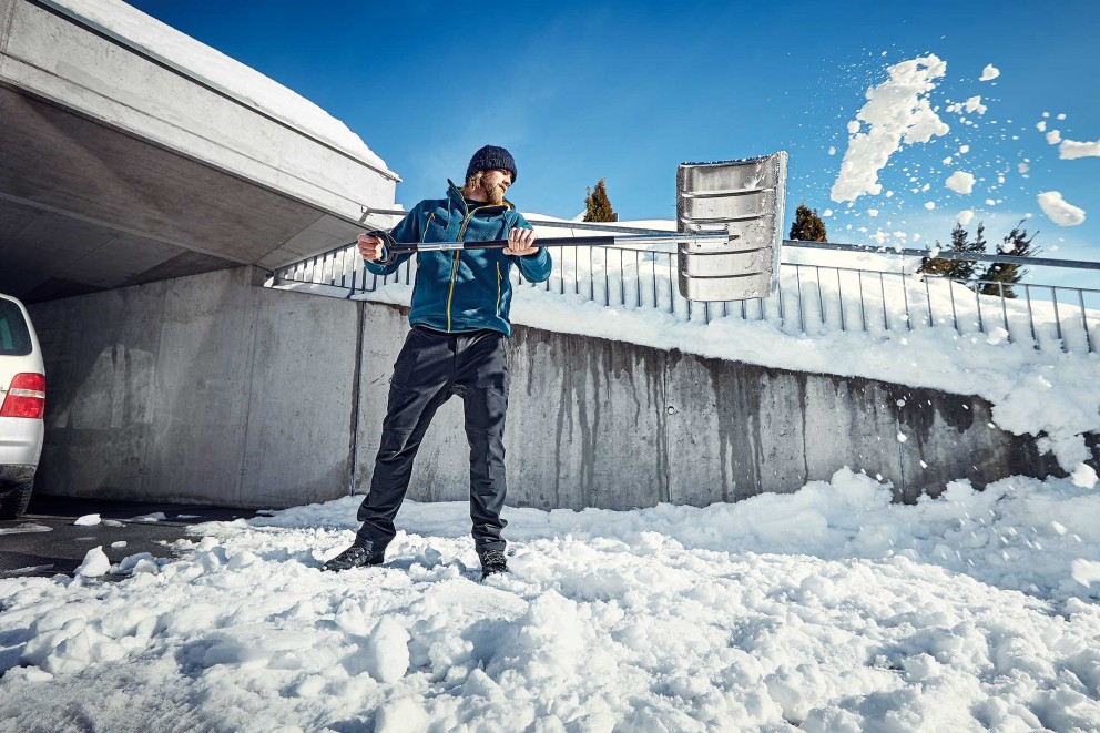 Man som skottar snö med en snöskyffel framför en betongvägg