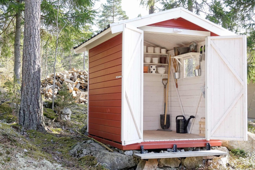 Trädgårdsskjul med öppna dörrar, trädgårdsredskap och växttillbehör