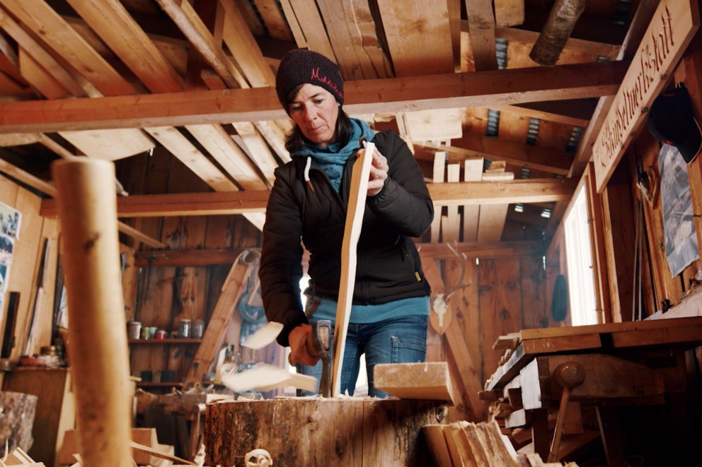 
				Eva Gredig bearbetar ett takspån med snickaryxan

			